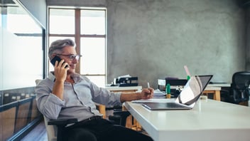 man on the phone to his advisor, smiling while taking notes
