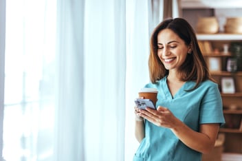 healthcare worker smiling at phone will holding a coffee